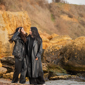Tender moment between a mother and daughter embracing by the sea. Love, warmth, and family connection captured in a candid outdoor portrait. Windy coastal scene with genuine emotions and happiness.