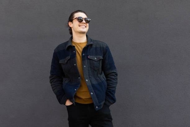 Trendy young man in sunglasses posing near the wall on the street on a summer day